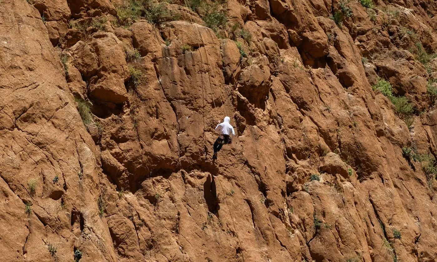 A person climbs a rugged, sunlit cliff face, illustrating adventure and nature's challenge.