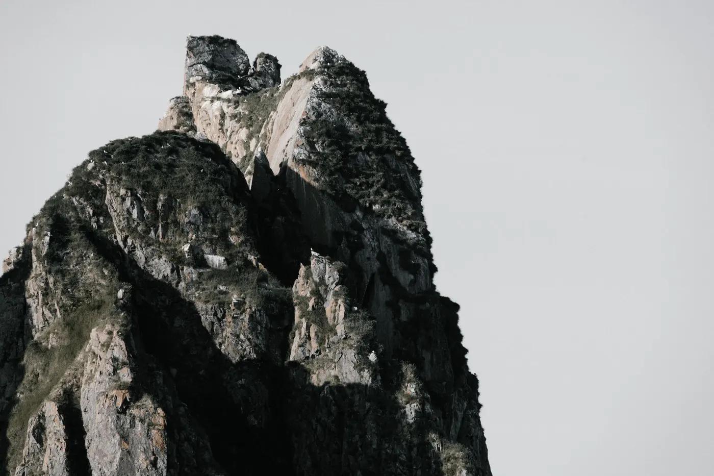 A stunning view of a rocky mountain peak under a clear, white sky, showcasing nature's raw beauty.