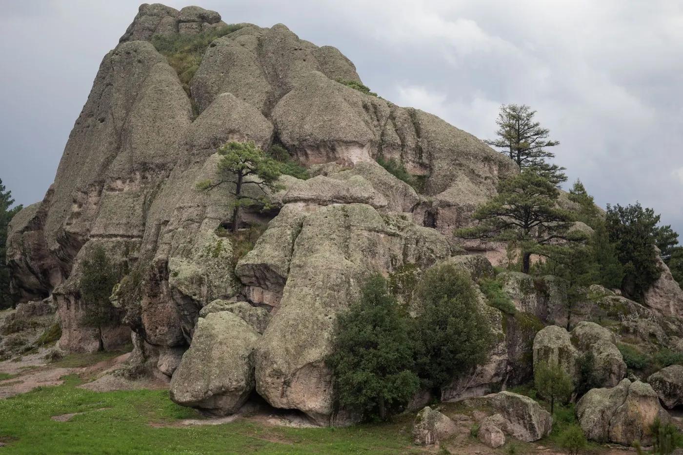 Dramatic rocky formation amidst lush greenery under a cloudy sky in Mexico.