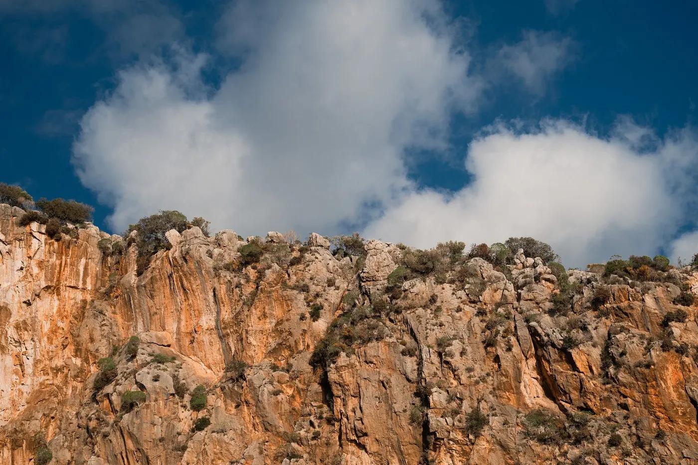 Majestic rocky cliffs under a bright blue sky with fluffy white clouds, capturing nature's grandeur.