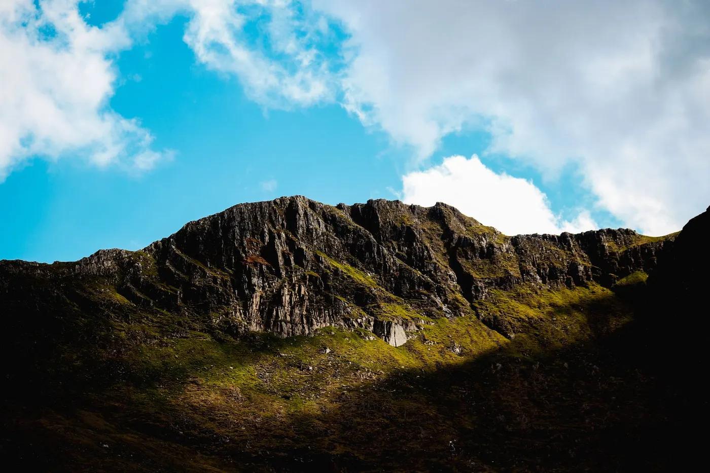 Captivating view of Welsh mountain peaks illuminated by sunlight, surrounded by vibrant blue sky and clouds.