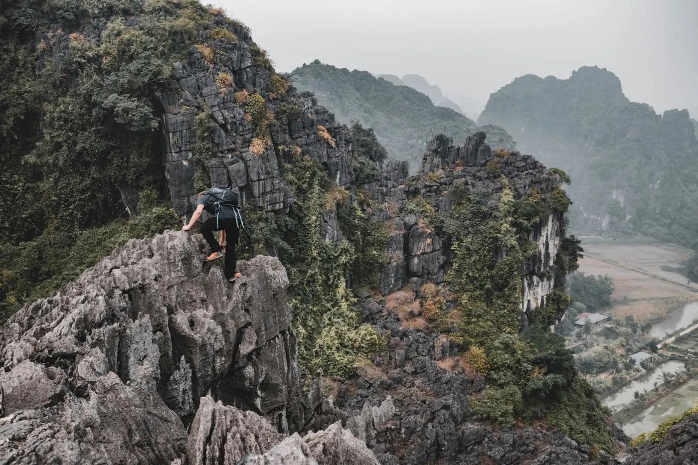 A hiker scales rugged limestone karsts in Hoa Lư, Vietnam, showcasing breathtaking natural beauty.