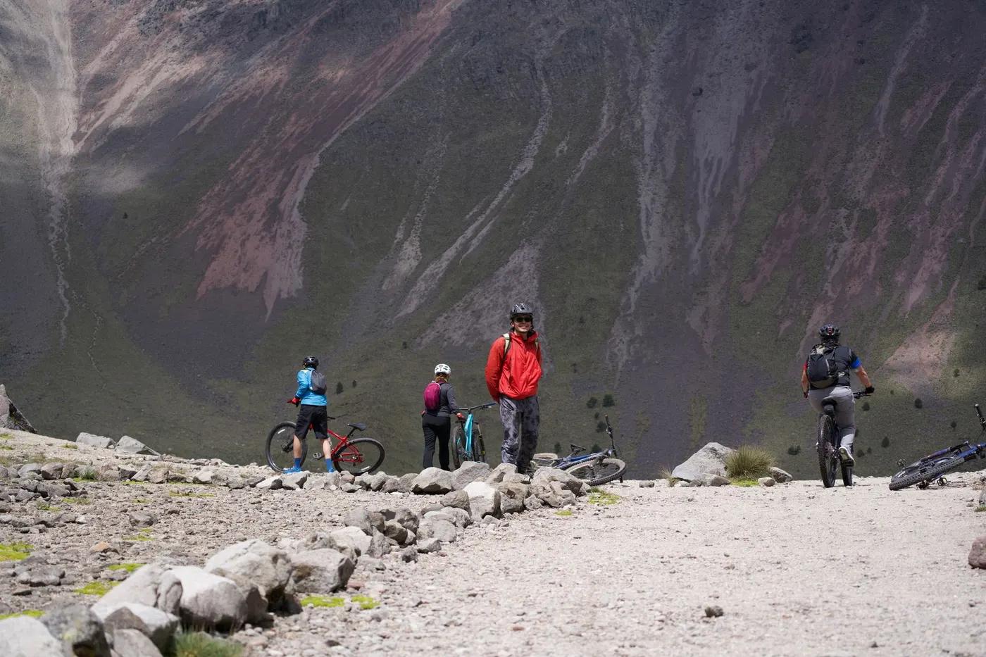 Group of cyclists mountain biking on a rugged hilltop trail amidst dramatic landscapes.