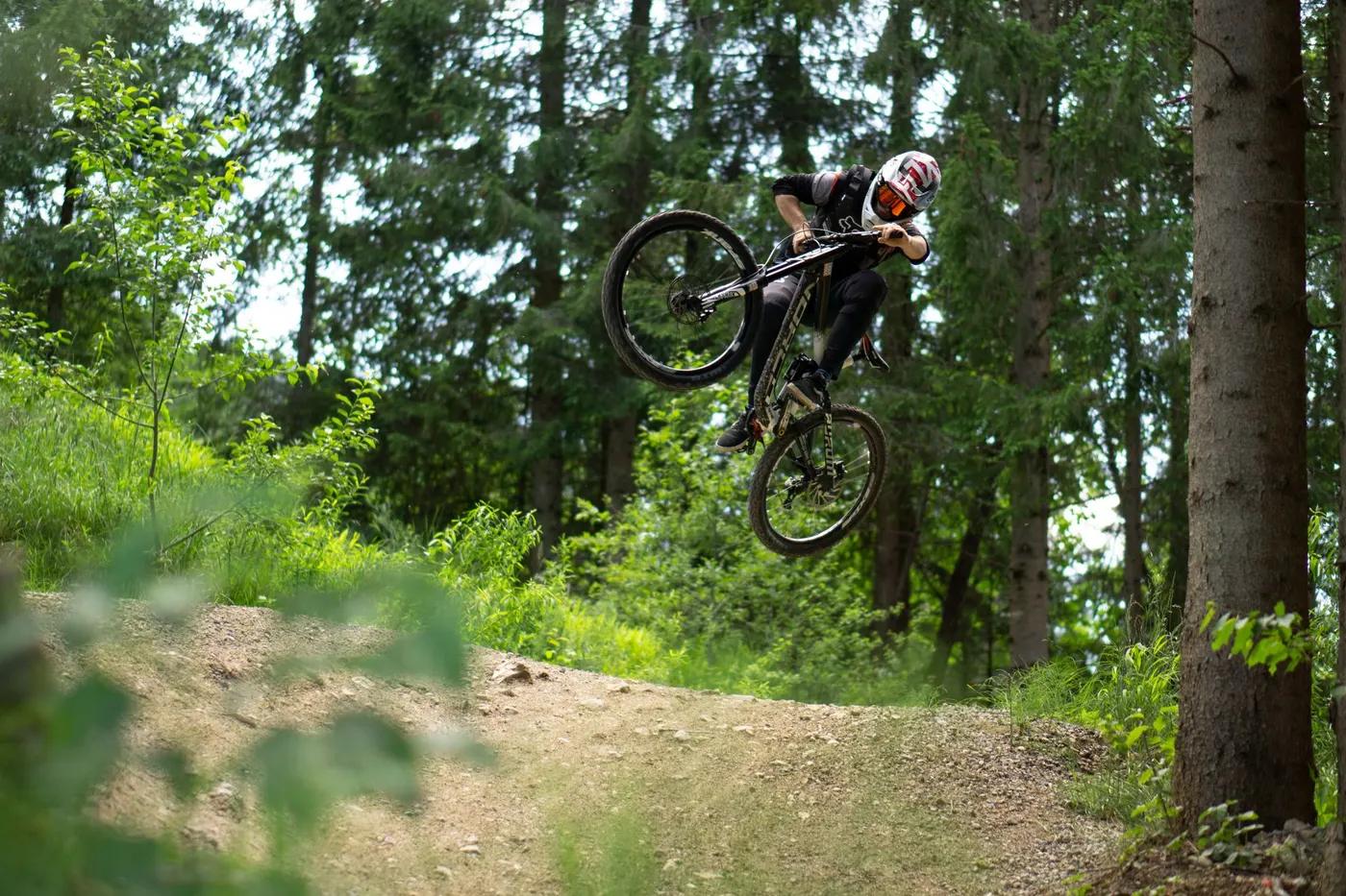 Dynamic shot of a mountain biker midair, surrounded by lush forest in Oberammergau, Germany.