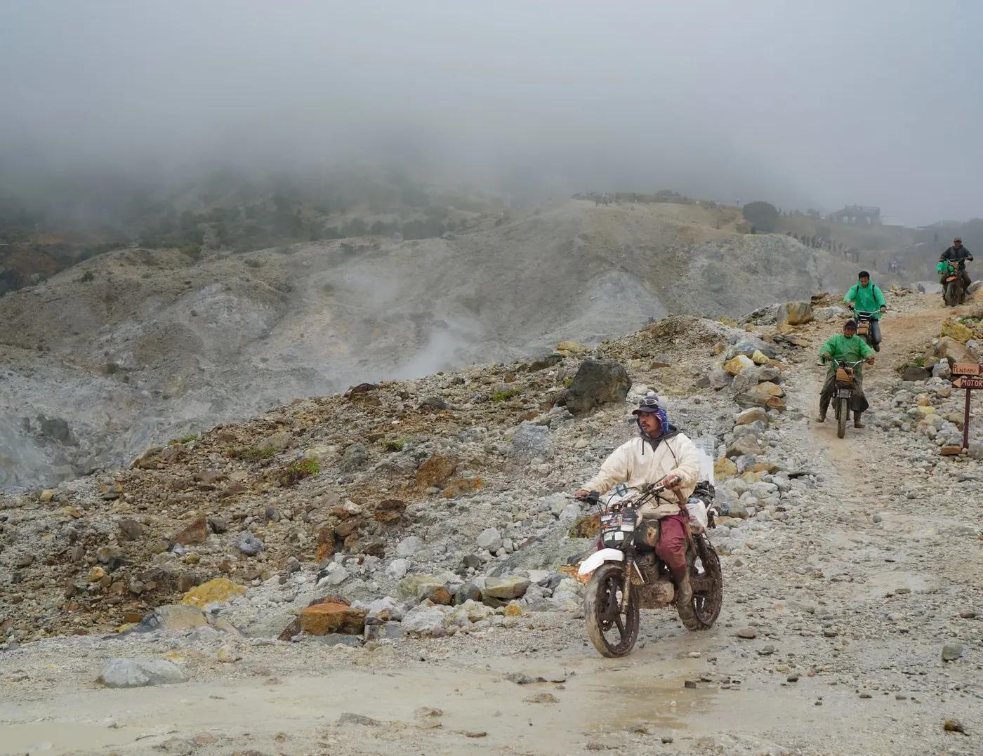 Daring motorcyclists ride over rocky terrain in foggy West Java hills.