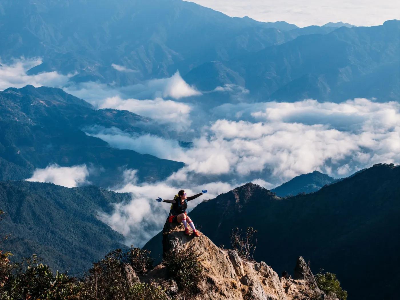 Hiker celebrates on a peak with stunning mountain and cloud views in Vietnam, capturing the spirit of adventure.
