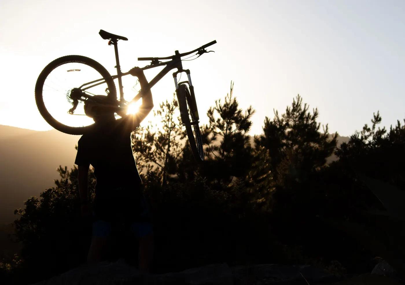 A cyclist lifts a mountain bike with enthusiasm against a sunset backdrop in San Luis Potosí, Mexico.