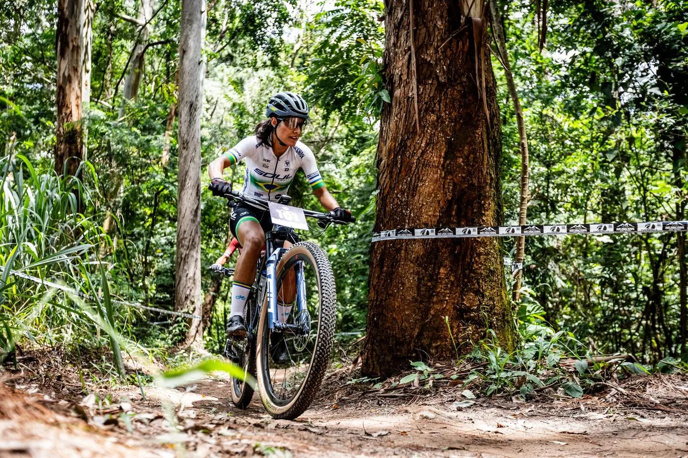 Female cyclist on mountain bike racing through a forest trail on a sunny day.