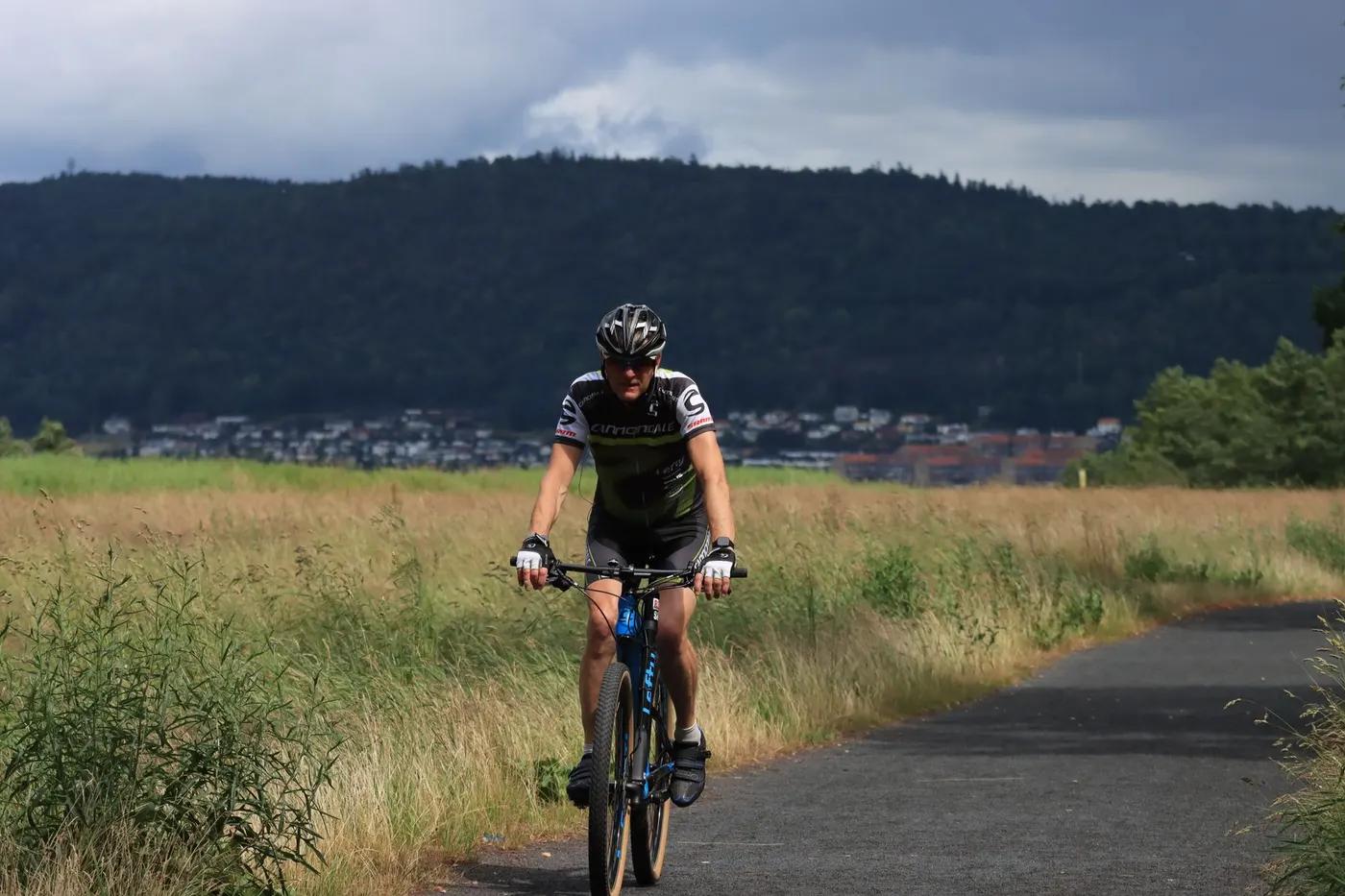 Mountain biker riding through a scenic trail in Huskvarna, Sweden with distant hills and a cloudy sky.