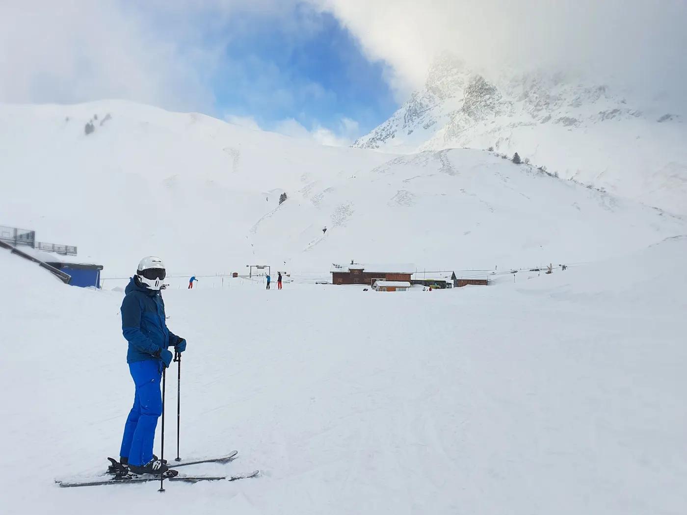 A skier pauses to admire the snow-capped mountains under a clear blue sky at a ski resort.