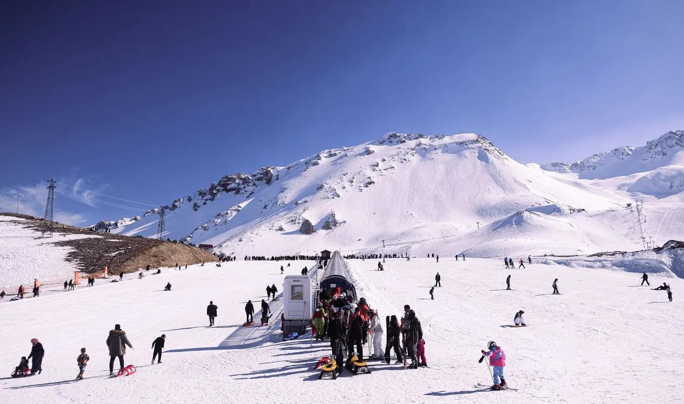 Scenic view of a bustling ski resort with snow-covered slopes and diverse group of skiers.