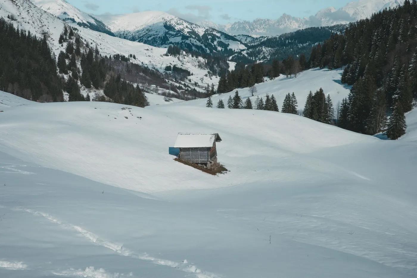 A solitary wooden cabin nestled in the snowy landscape of the French Alps in winter.