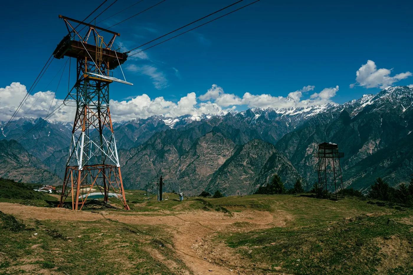 Experience the breathtaking snow-capped peaks of Auli, Uttarakhand, India, with a prominent cable tower in the foregrou…
