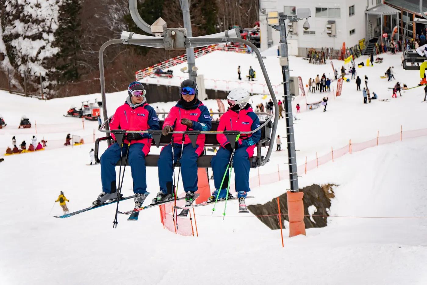 Three skiers in vibrant attire on a ski lift in Yuzawa, Japan, winter sports scene.