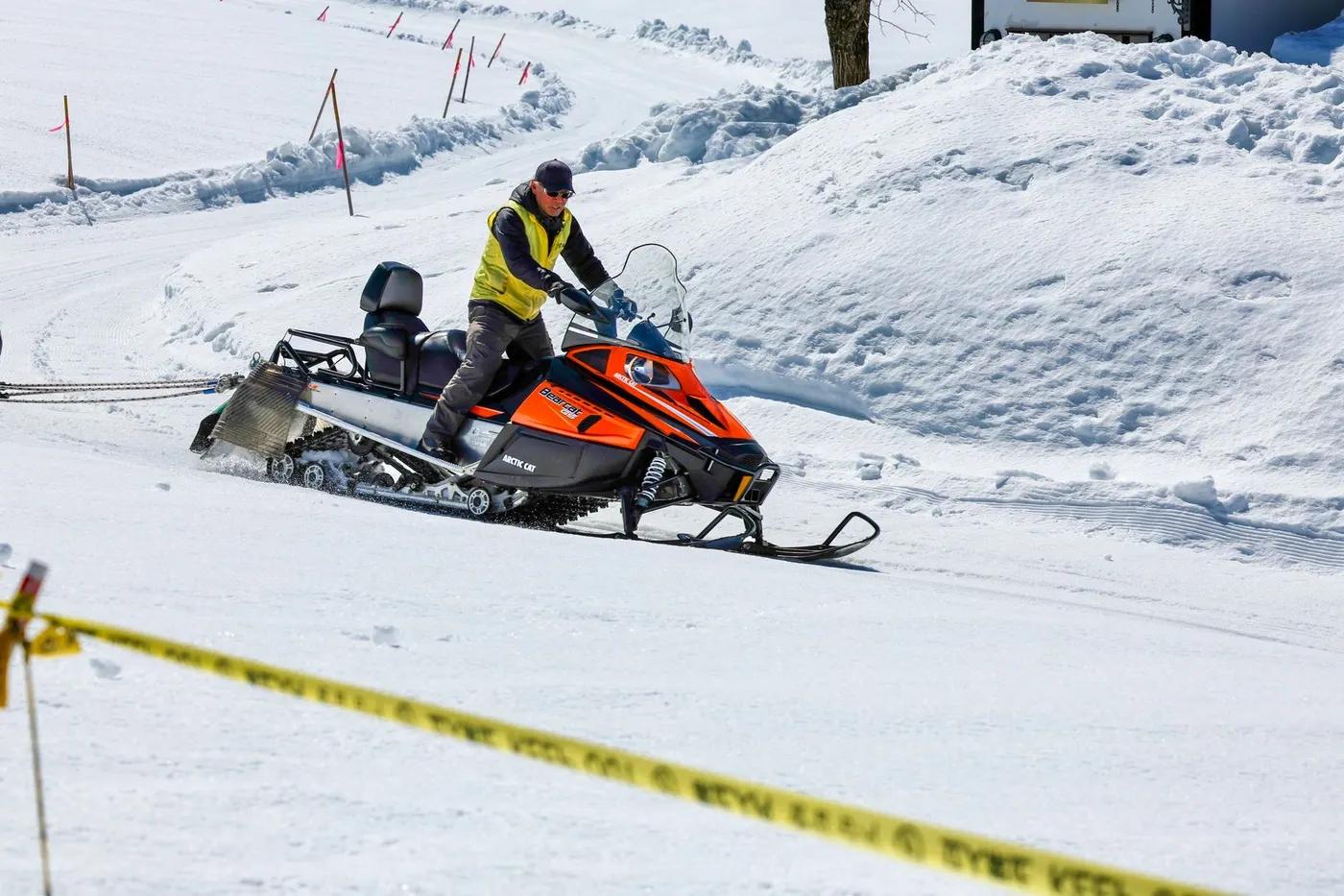 A man on an orange snowmobile traverses a snowy terrain in Hokkaido, Japan.