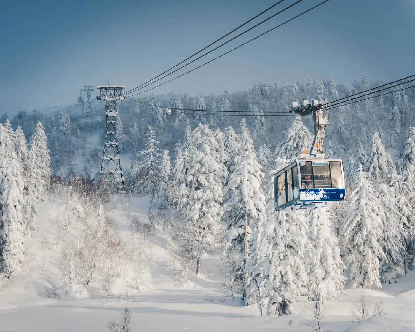 A scenic cable car ride over a snow-blanketed forested mountain landscape during winter.