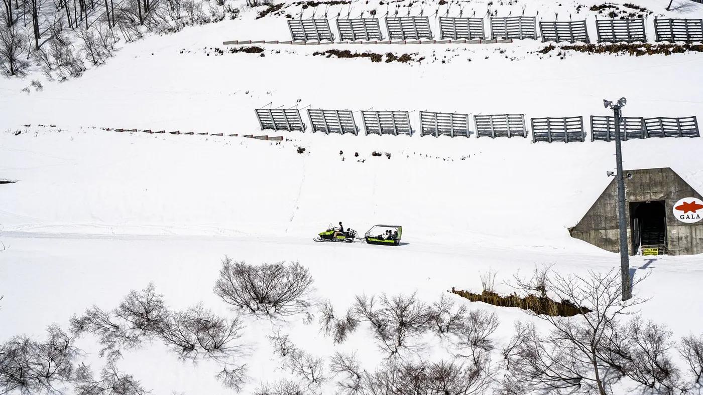 Aerial view of snow-covered landscape with snowmobiles near a bunker entrance in winter.