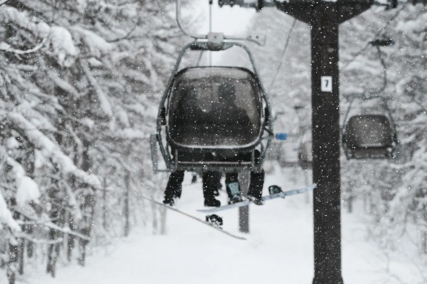 Skiers on a lift in a snowy forest in Japan, embracing the winter wonderland.