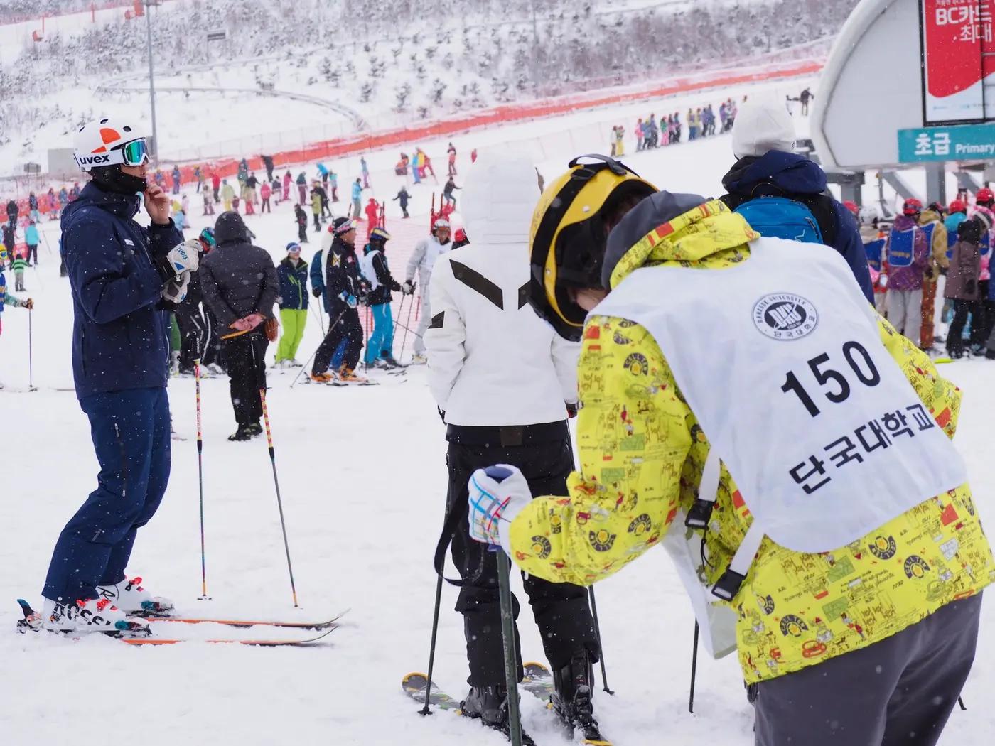 Crowded ski resort scene with people in colorful winter attire skiing and enjoying the snowy slopes.