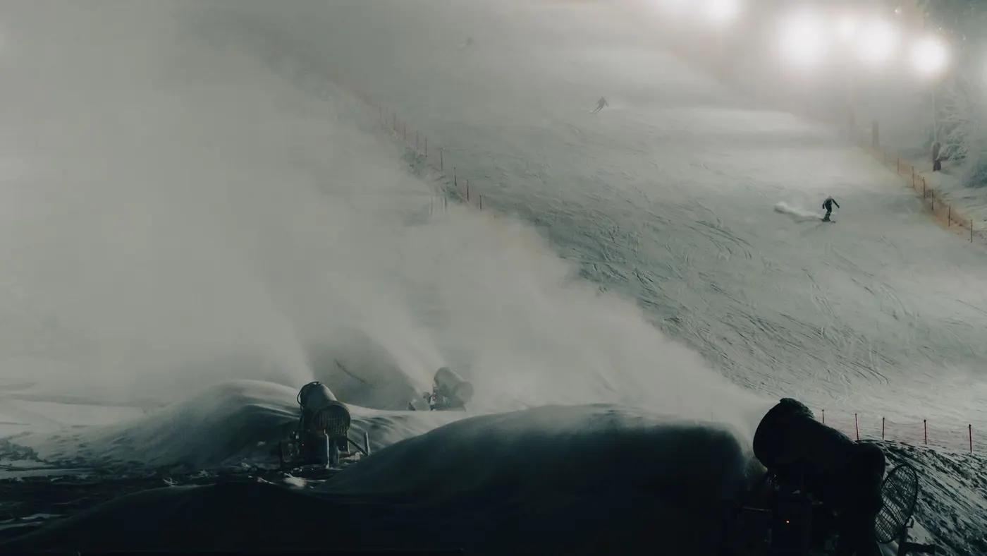 Skier on a snowy slope at night with lit snow cannons and a wintery atmosphere.