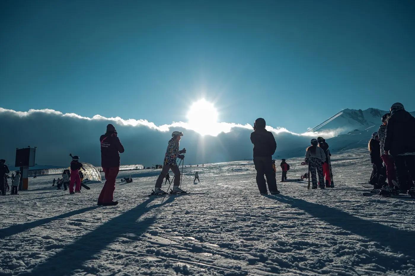 Skiers gather on a snowy mountain slope during a sunny winter morning, showcasing a vibrant ski resort scene.