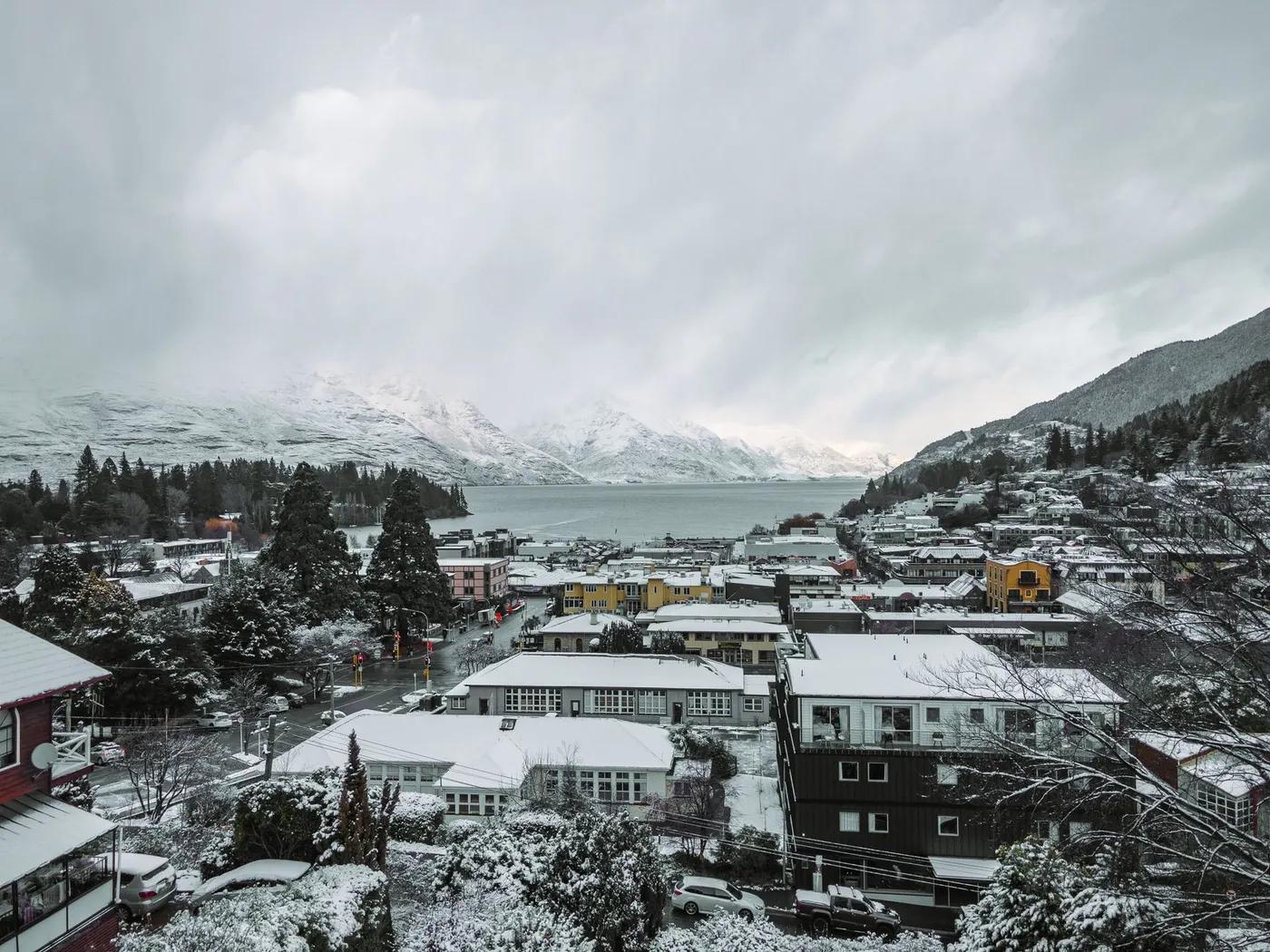 A stunning aerial winter view of Queenstown, New Zealand, showcasing snow-covered buildings and Lake Wakatipu.