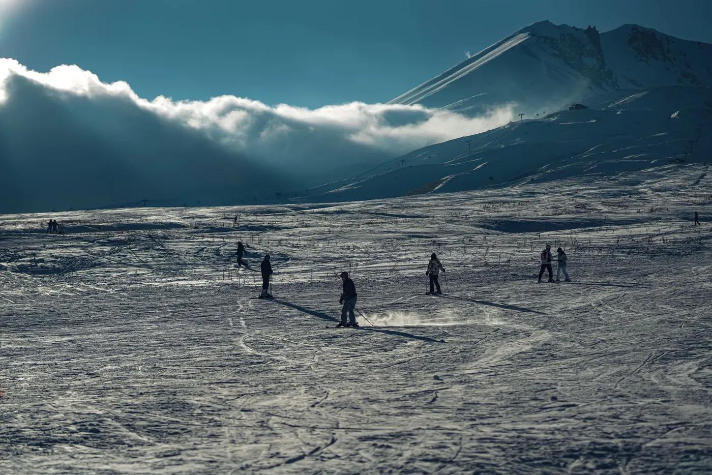 Skiers enjoying a calm, winter morning on a snowy mountain slope with a dramatic sky.