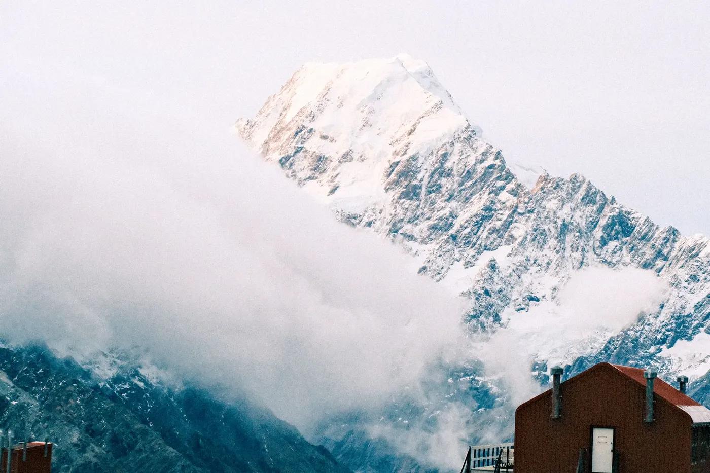 Majestic Aoraki Mount Cook in New Zealand, engulfed by clouds, offering a breathtaking snowy spectacle.