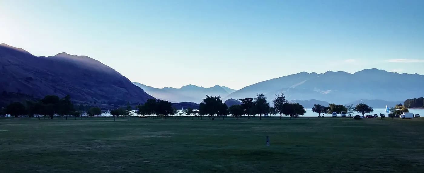 Peaceful landscape featuring mountains, a lake, and trees in Queenstown, New Zealand.