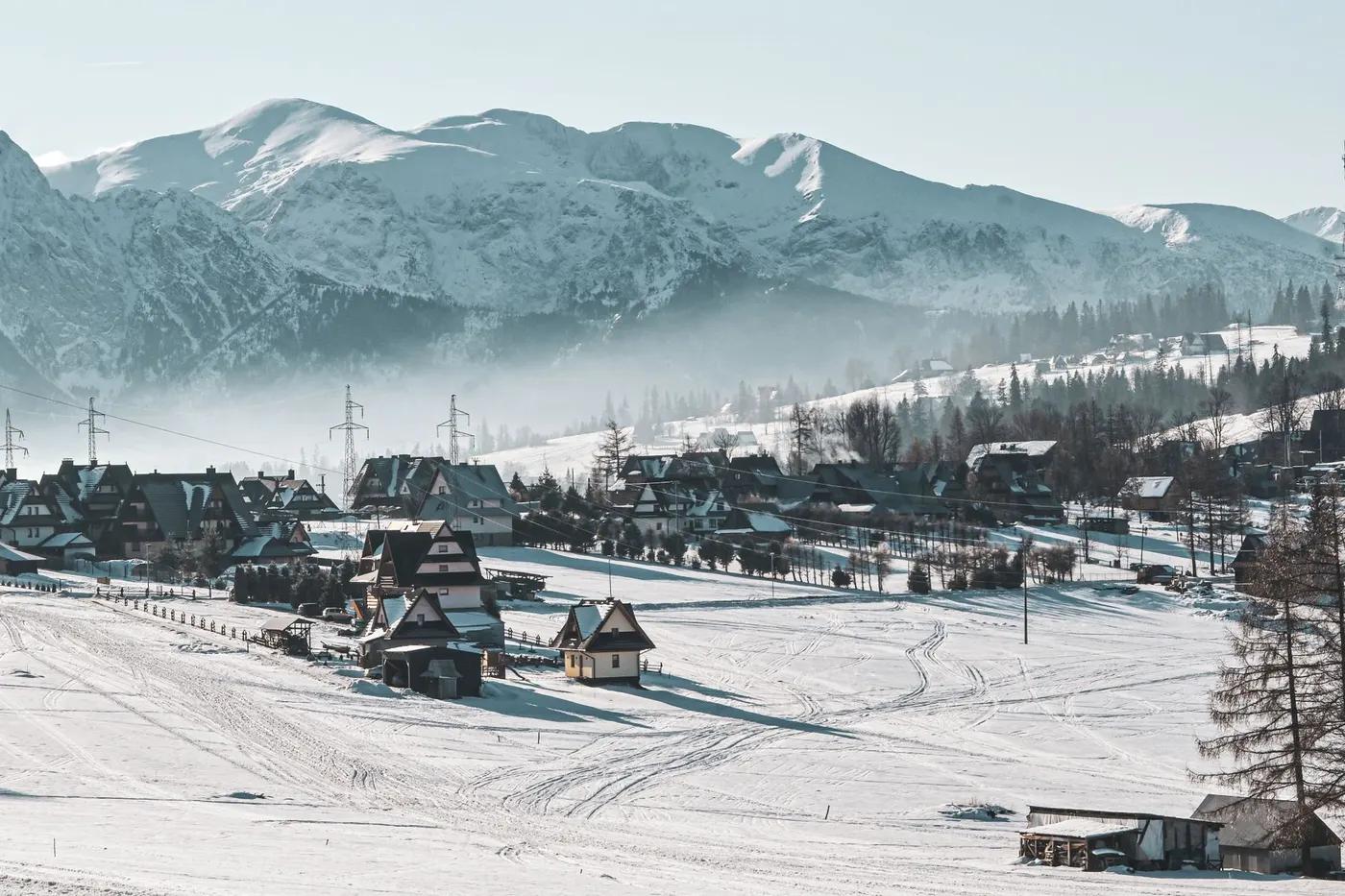 Snow-covered village with mountain backdrop in winter, Zakopane, Poland.