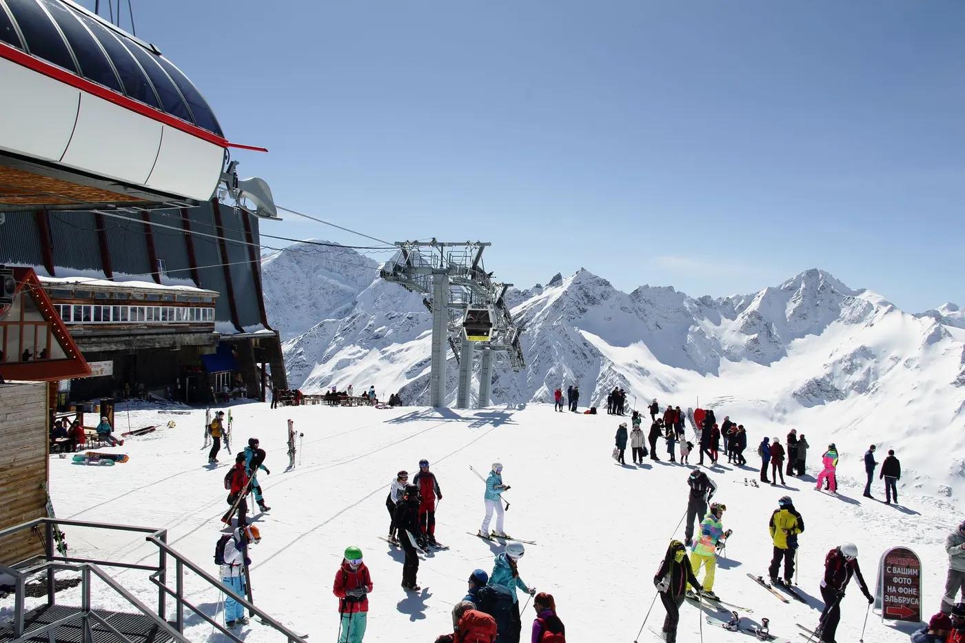 Tourists enjoying a sunny day at a snow-covered ski resort in Russia's Caucasus mountains.