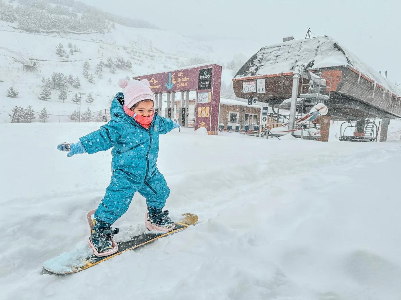 A young child joyfully snowboarding at a snowy mountain resort in winter.