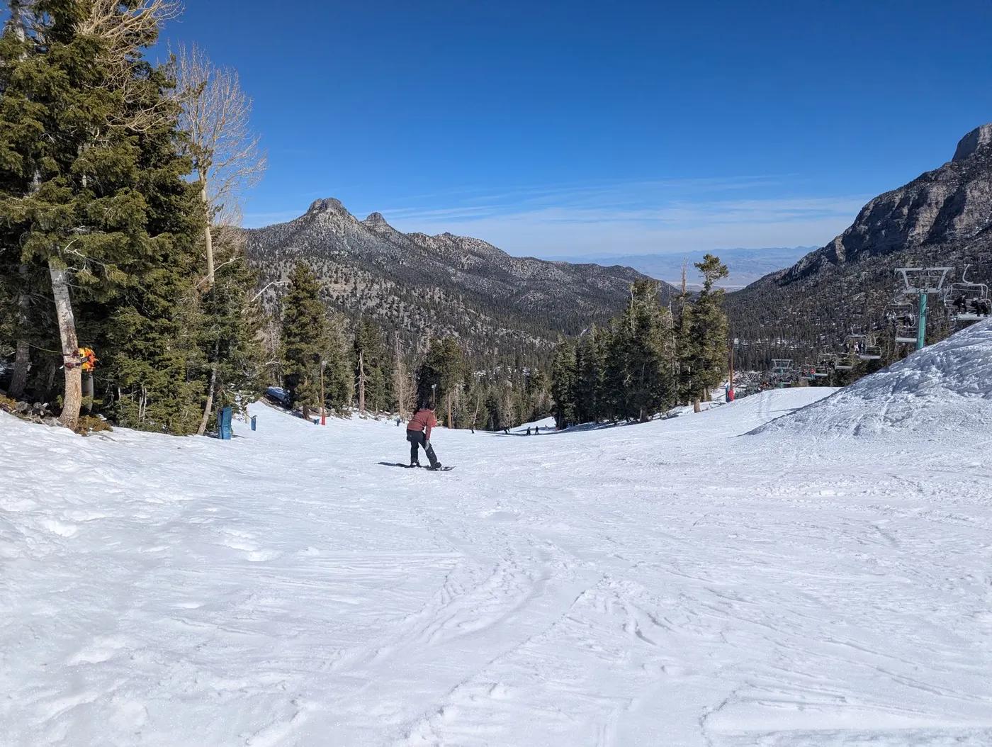 A skier glides down a snowy slope at Mount Charleston, NV, surrounded by scenic mountain views.
