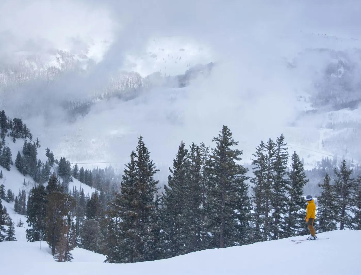 A skier in a yellow jacket enjoys a snowy day at Brighton Resort, Utah's alpine landscape.