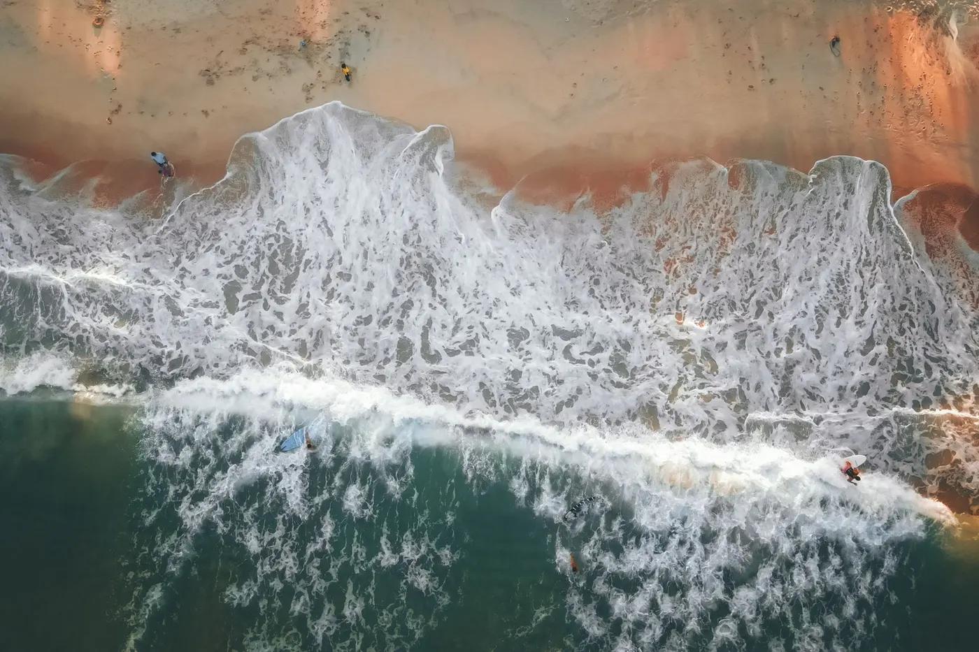 Aerial shot of surfers riding waves along a sandy beach in Terengganu, Malaysia.