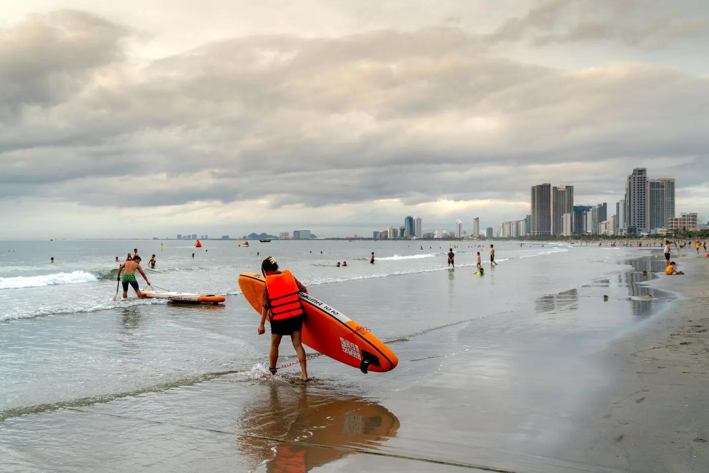 Beachgoers surfing at sunset with city skyline in the background.