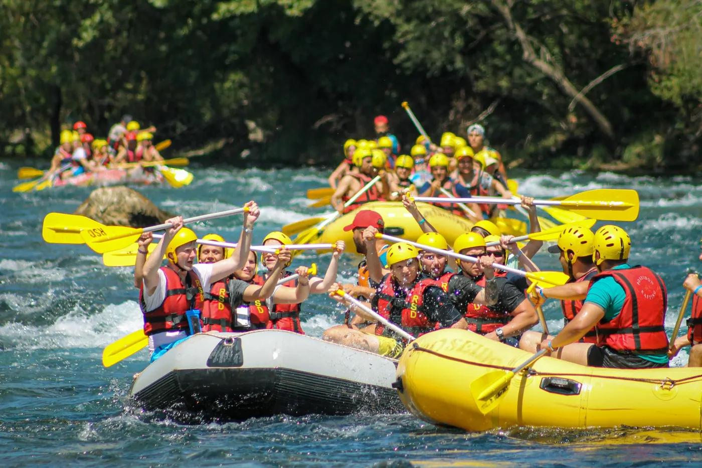 Teams of rafters navigate rapids in colorful inflatable boats on a sunny day, showcasing teamwork and thrill.